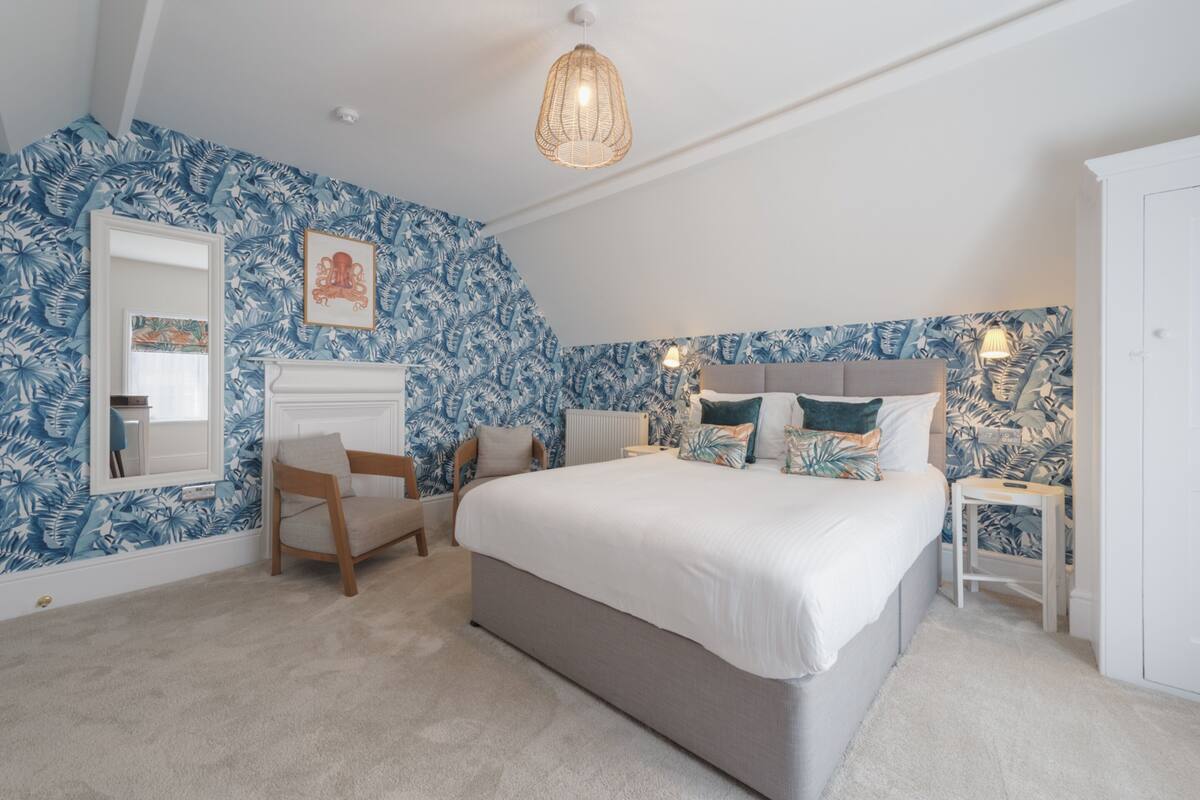 A bedroom with a large bed, a chair, a nightstand, and a dresser.