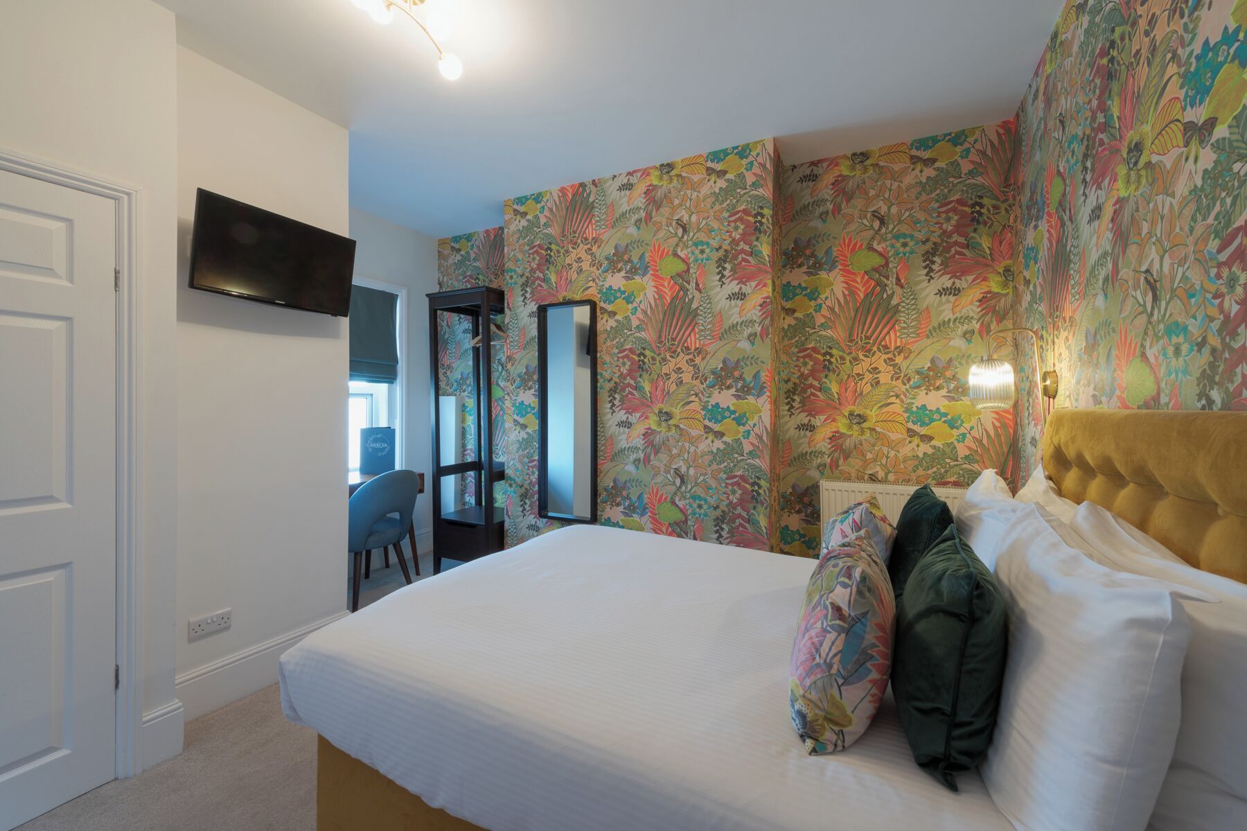 A bedroom with a bed, a TV mounted on the wall, and a floral wallpaper.