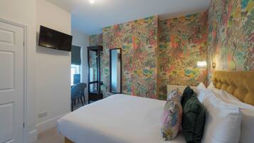 A bedroom with a bed, a TV mounted on the wall, and a floral wallpaper.
