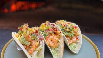 Three tacos on a plate with a pizza oven in the background.