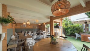 Um restaurante acolhedor com mesas e cadeiras de madeira, plantas pendentes e uma luminária trançada grande.