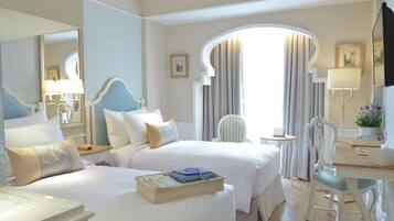 A hotel room with two beds, a desk, a chair, and a large window with curtains.