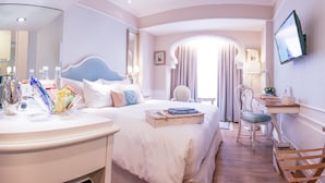 A hotel room with a bed, bedside table, chair, desk, and TV. - Noor Hotel (Bandung)
