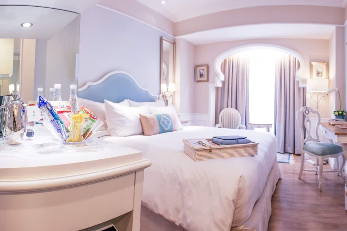 A hotel room with a bed, bedside table, chair, desk, and TV.