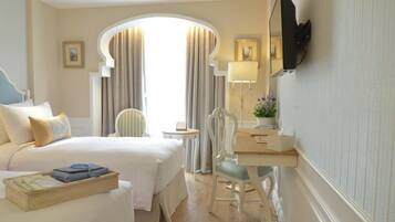 Quarto de hotel com cama, escrivaninha, cadeira, televisão e janela com cortinas.