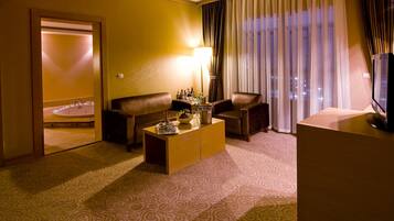 Habitación de hotel con sofá, una mesita, televisor y vistas a la ciudad a través de amplias ventanas.
