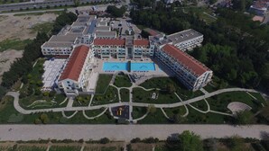 Vue aérienne d’un grand complexe hôtelier moderne, composé de plusieurs bâtiments, doté d’une piscine centrale et de jardins bien entretenus.