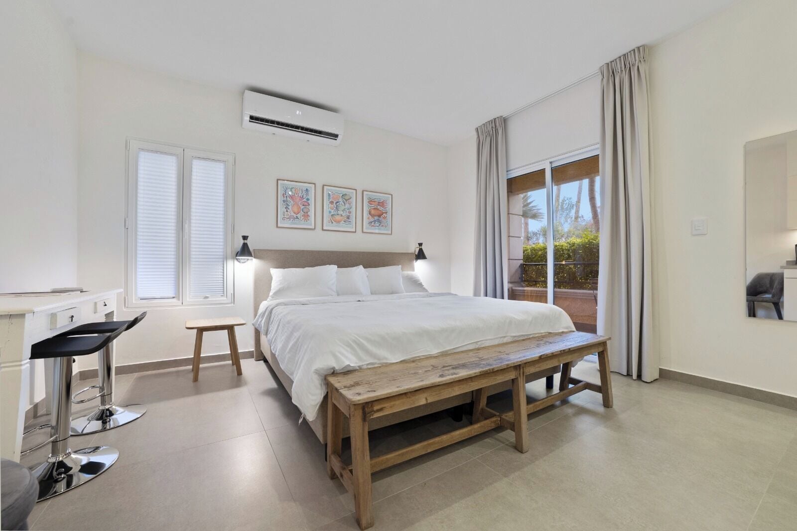 Un dormitorio con cama, escritorio, banca y ventana con cortinas.