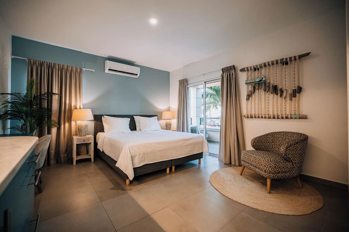 A modern hotel room with a bed, bedside tables, a chair, and a view of the outdoors.