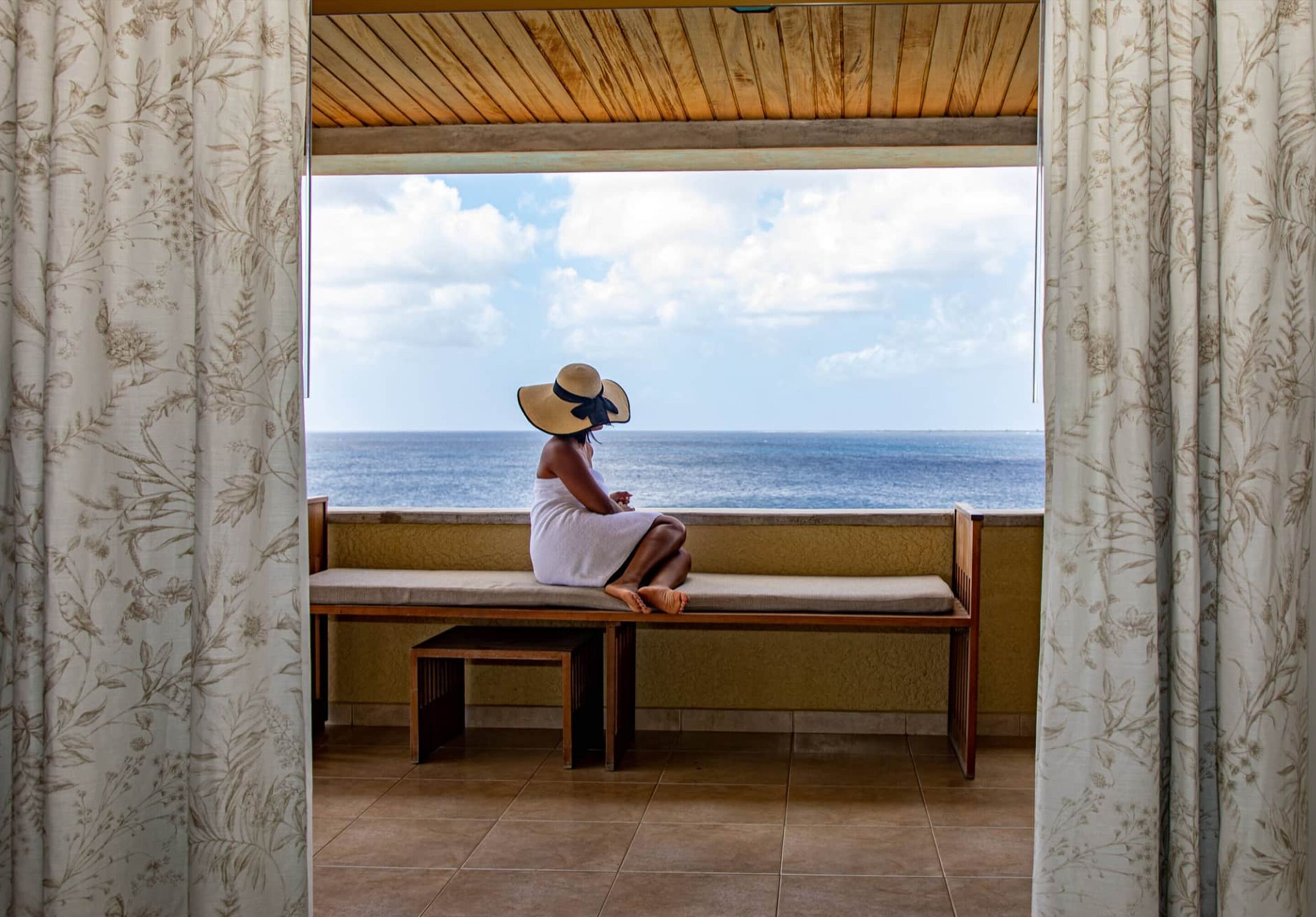 A person sitting on a bench by a window with a view of the sea.