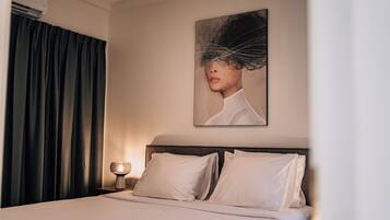 Una habitación de hotel con una cama, una mesita de noche con lámpara, un cuadro en la pared y cortinas oscuras.