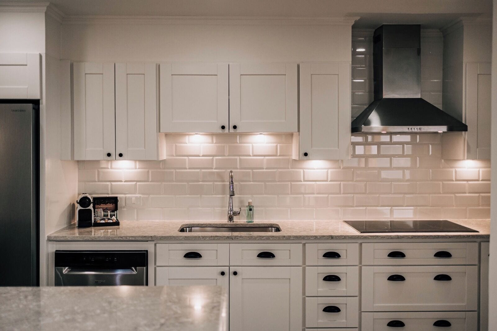 A modern kitchen with white cabinetry, a stainless steel dishwasher, a built-in oven, and a black range hood.