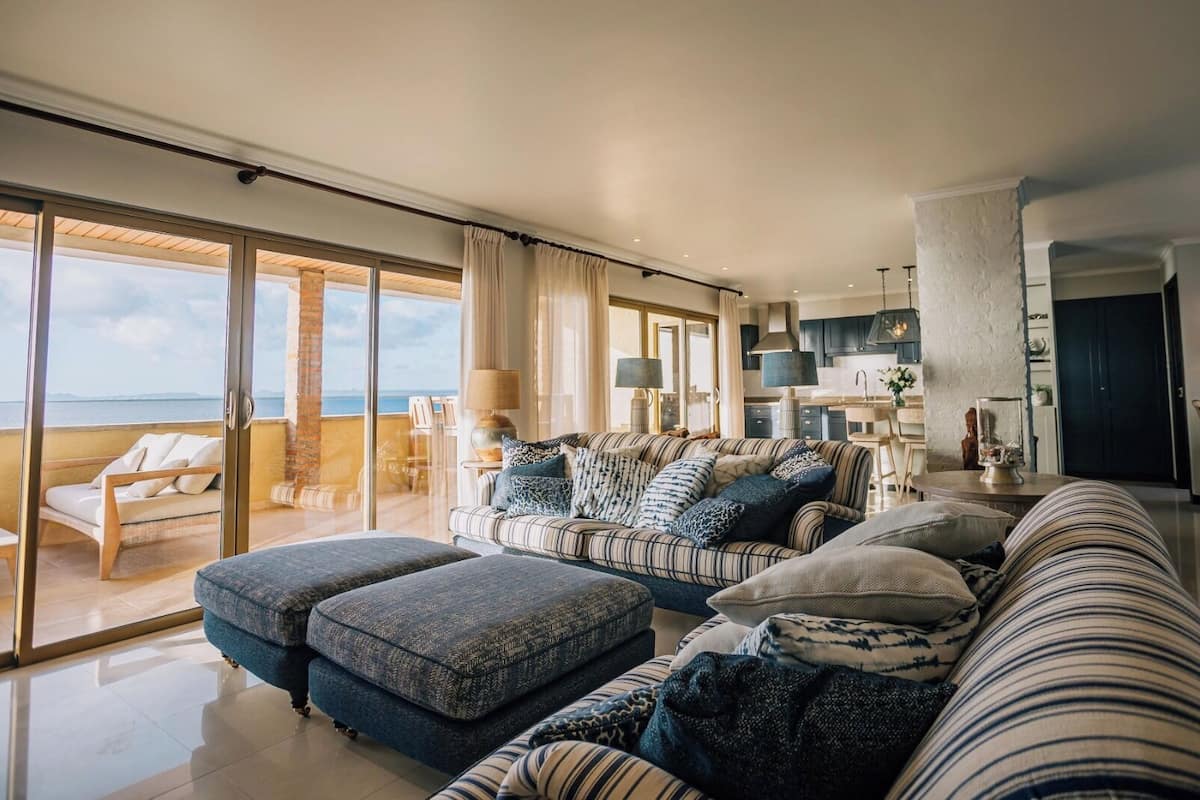A spacious living area with a large sofa set, a coffee table, and a view of the sea through large sliding glass doors.