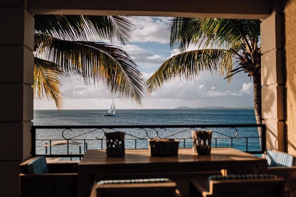 Un balcón con vista al mar, palmeras y un velero.