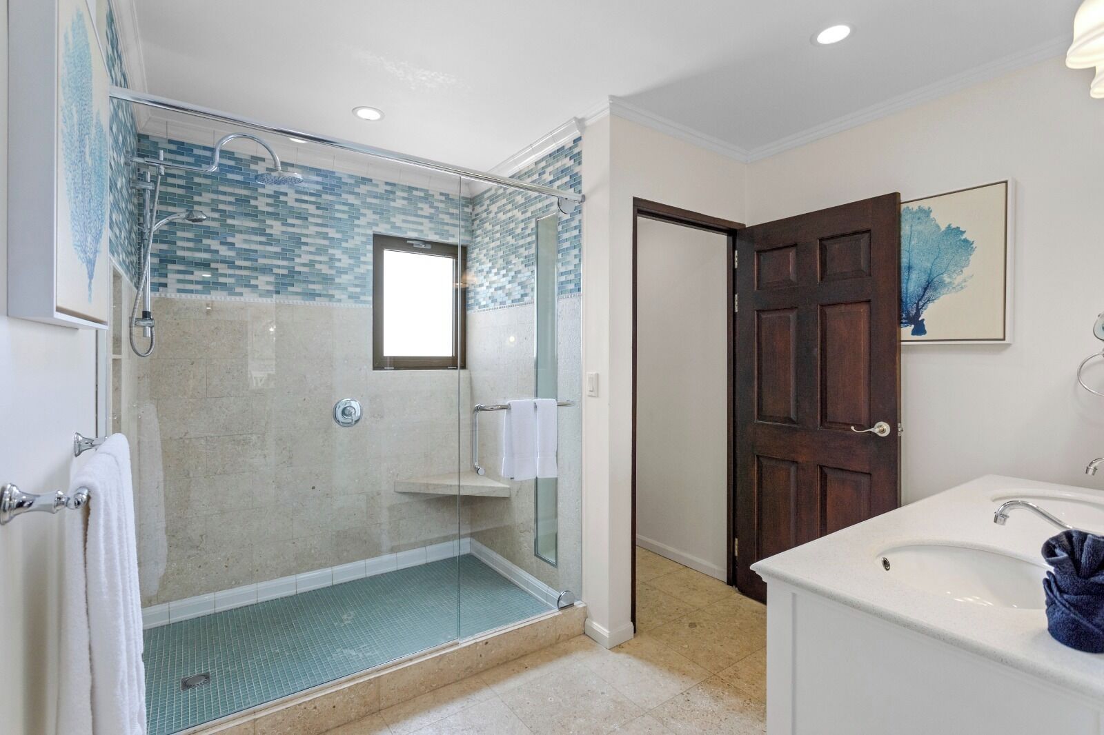 A modern bathroom with a glass-enclosed shower, a white sink, and a wooden door.
