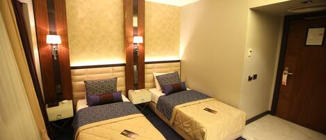 A hotel room with two beds, each with a headboard, bedside tables, lamps, and a small nightstand.