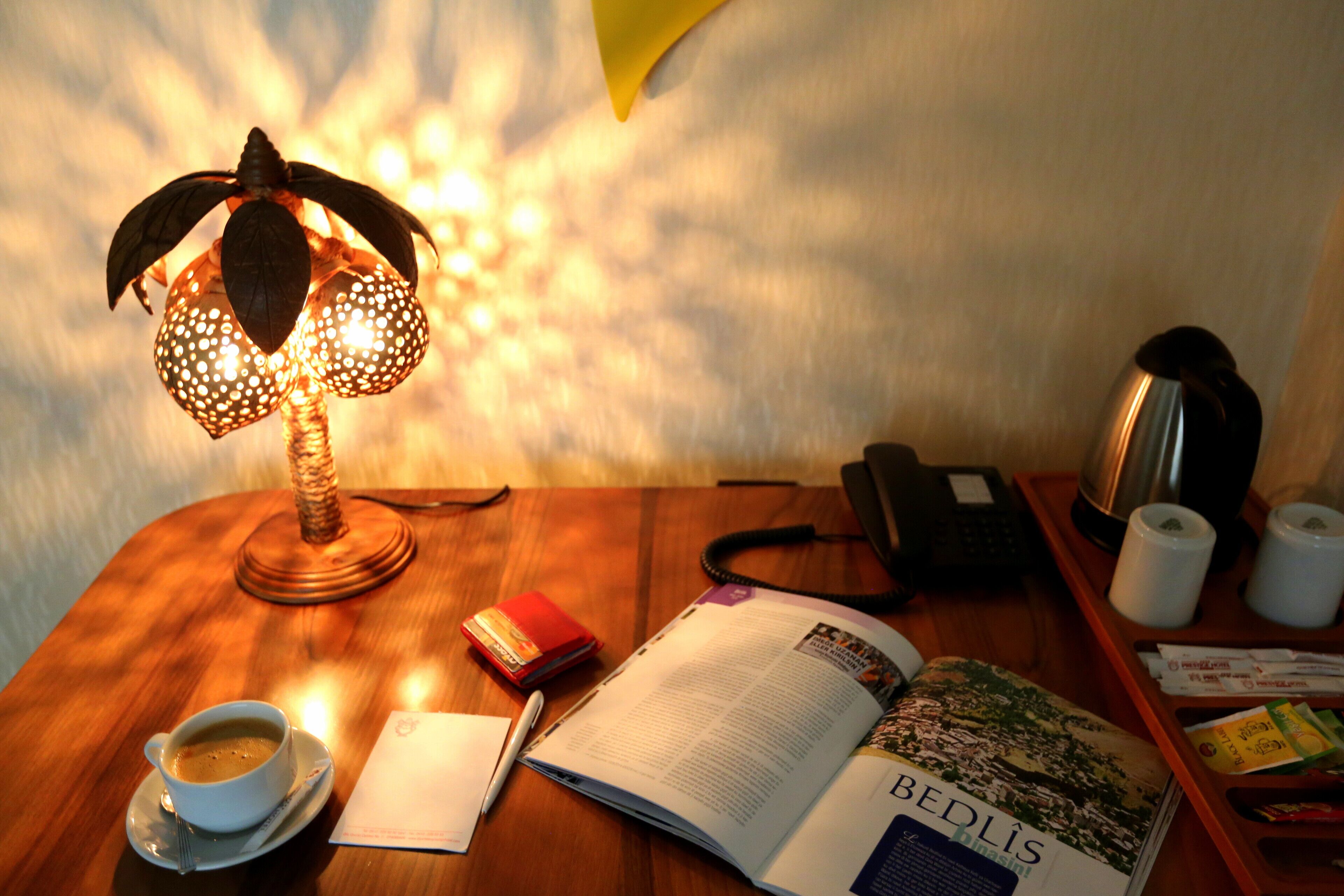 Ein Holztisch mit einer Lampe, einer Kaffeetasse, einem Buch, einem Notizblock und einem Telefon.