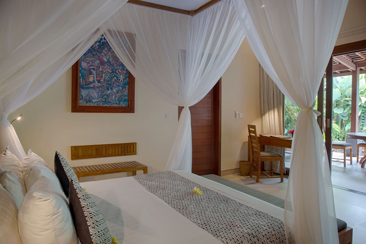 Un dormitorio con cama, un banco de madera, una mesa de comedor con sillas y un cuadro en la pared.