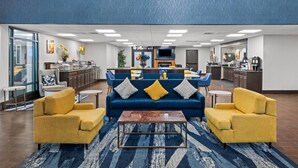 Un vestíbulo moderno con un conjunto de sofá azul, sillones amarillos, una barra de café y un bar deportivo.