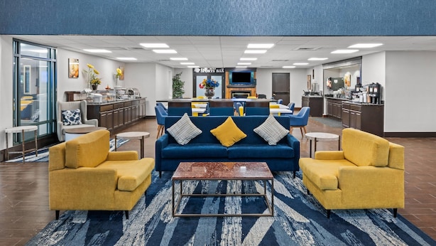 A modern lobby with a blue sofa set, yellow armchairs, a coffee bar, and a sports bar.