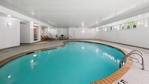 An indoor swimming pool with clear water, surrounded by white walls and a tiled floor.