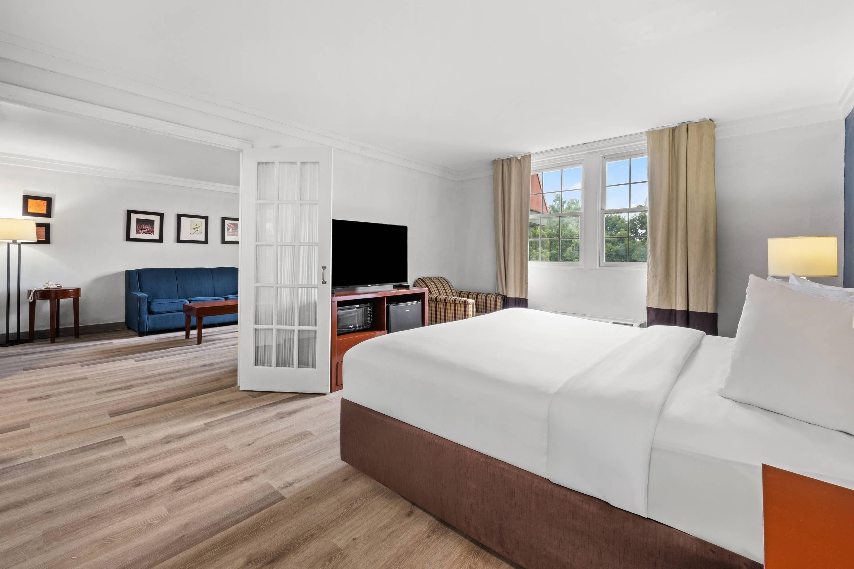 A hotel room with a large bed, a TV, a sofa, a dining table, and a kitchen area.