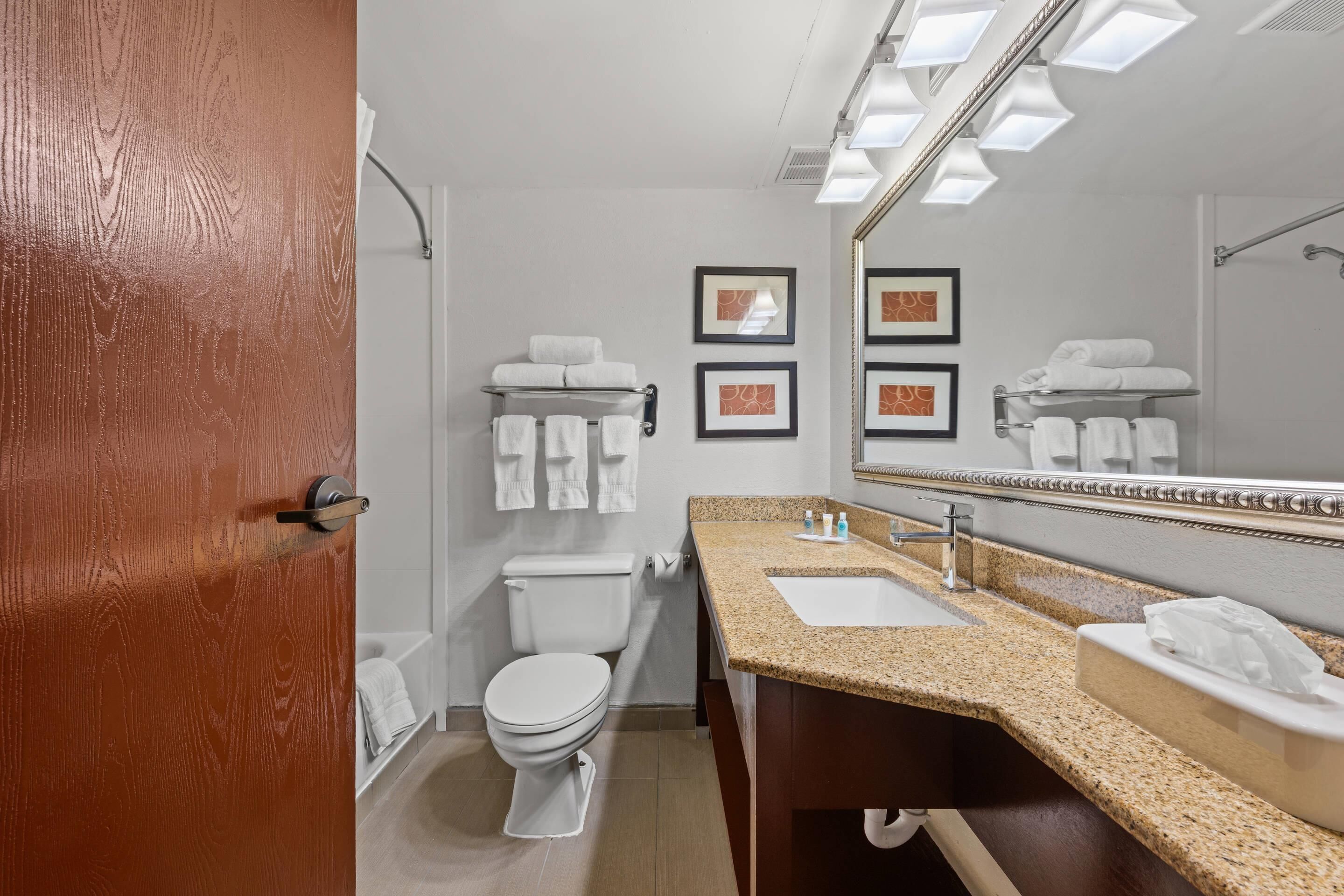 A modern bathroom with a toilet, sink, and mirror. There are towels on the wall and a door with a wooden frame.