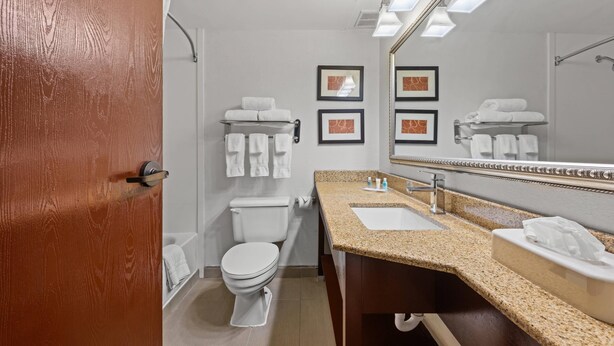 Un baño moderno con inodoro, lavabo y espejo. Hay toallas en la pared y una puerta con marco de madera.