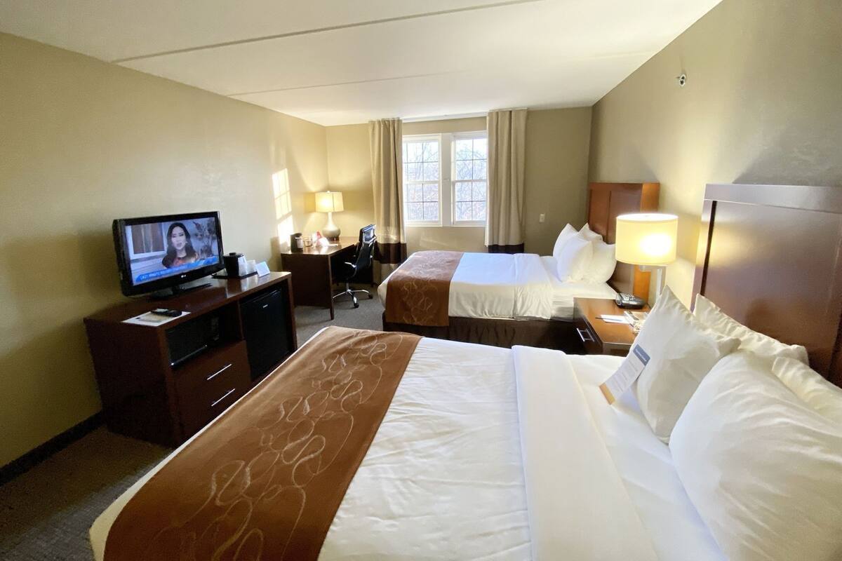 Une chambre d’hôtel avec deux lits, un bureau avec une télévision, une chaise et une lampe.