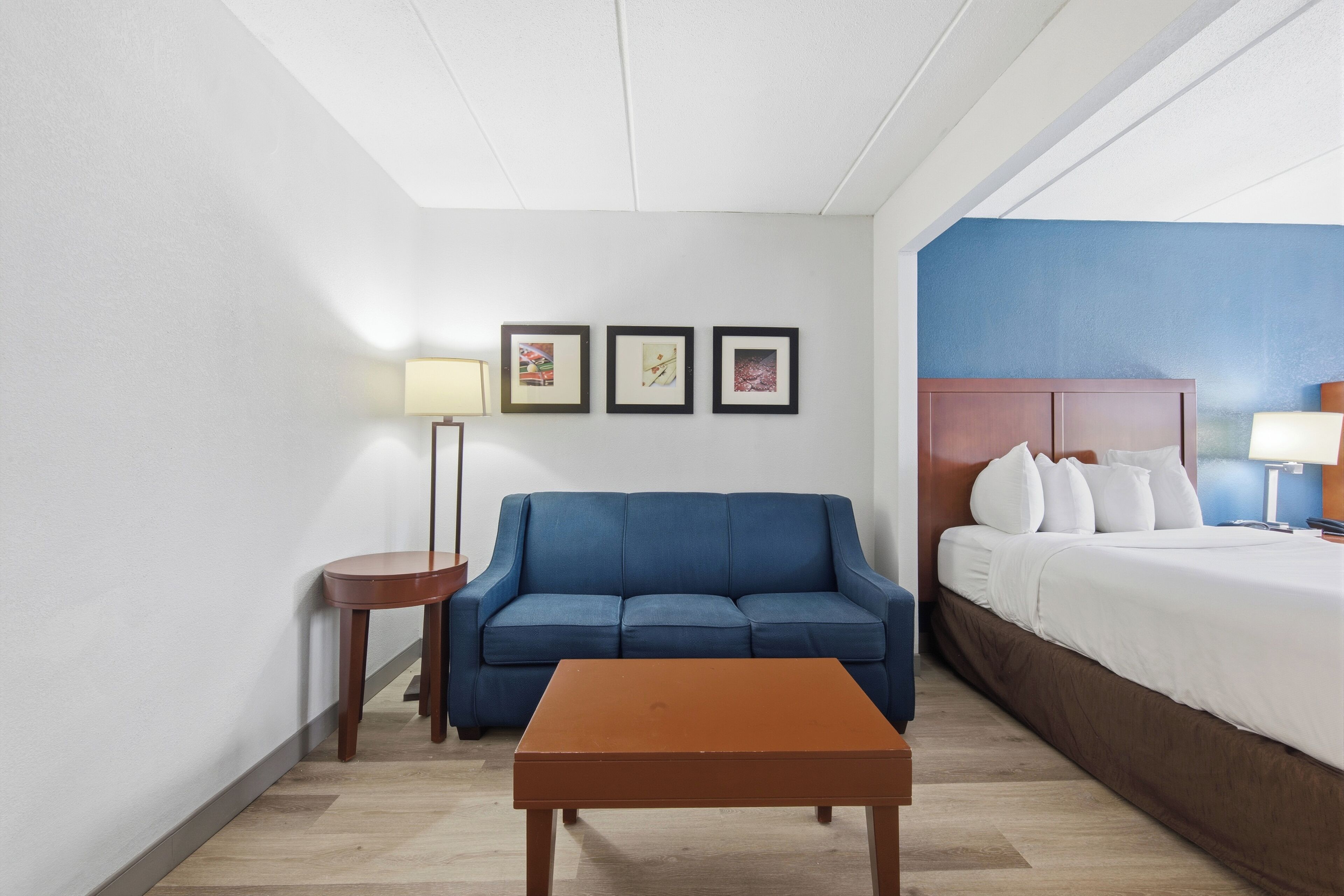 Een hotelkamer met een blauwe bank, een houten tafel, een bed met witte lakens en drie ingelijste foto's aan de muur.
