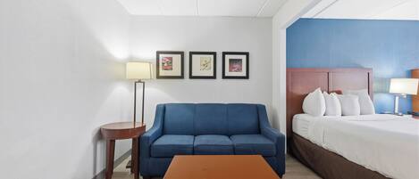 Habitación de hotel con sofá azul, una mesa de madera, una cama con ropa de cama blanca y tres cuadros en la pared.