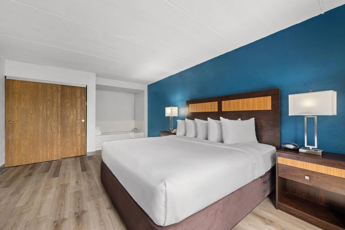 Een moderne hotelkamer met een groot bed, een houten hoofdbord, twee nachtkastjes met lampen, een houten garderobe en een blauwe accentmuur.