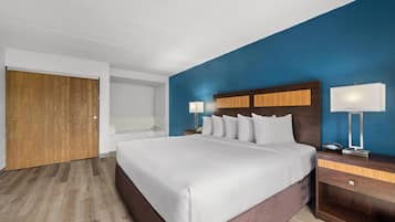 A modern hotel room with a large bed, wooden headboard, two bedside tables with lamps, a wooden wardrobe, and a blue accent wall.