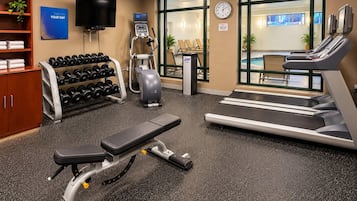 A gym with exercise equipment, a television, and a clock on the wall.