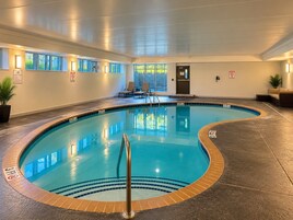Una piscina interior con borde de azulejos, un puesto de socorrista y una puerta que da al exterior.