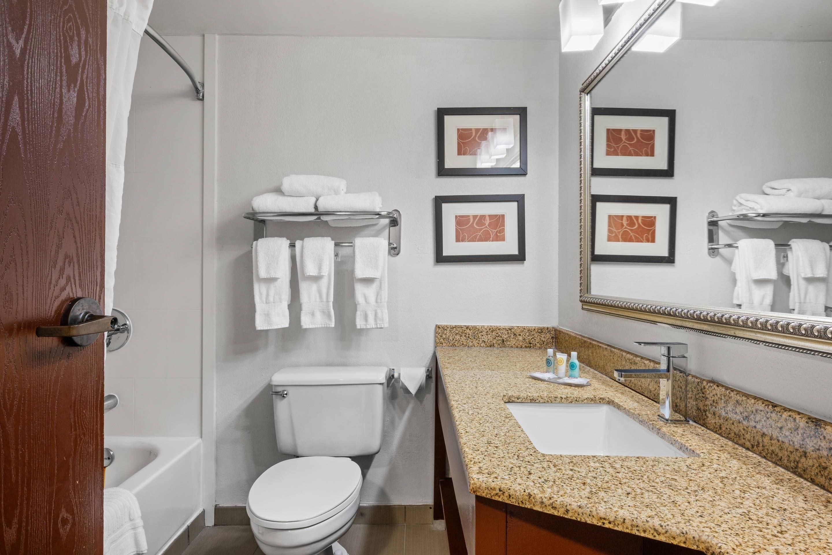 A bathroom with a toilet, sink, and bathtub. There are towels on a rack and framed pictures on the wall.