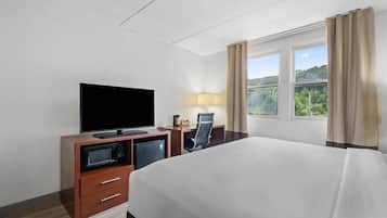 Hotelkamer met een bed, een televisie, een bureau met lamp en uitzicht op groen.