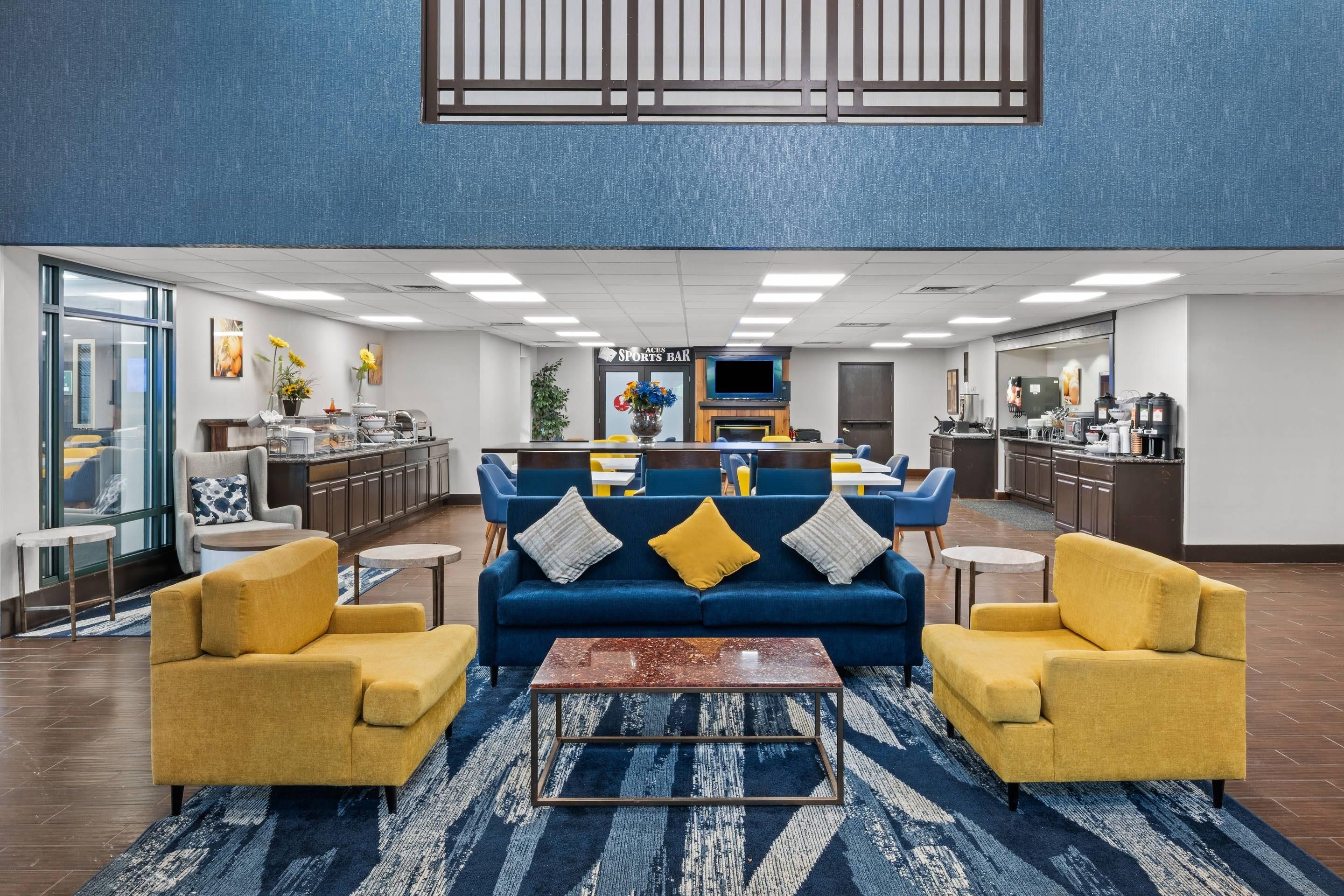A modern lobby with a blue sofa set, yellow armchairs, a coffee bar, and a sports bar.