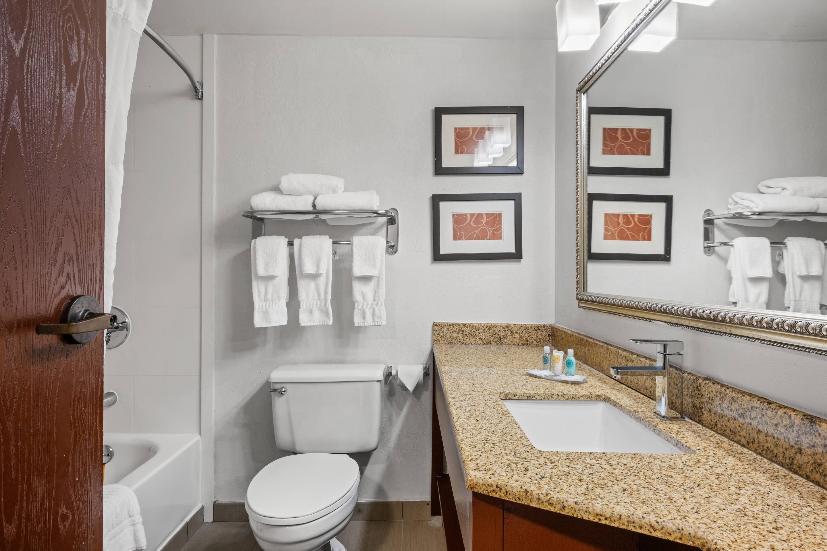 A bathroom with a toilet, sink, and bathtub. There are towels on a rack and framed pictures on the wall.