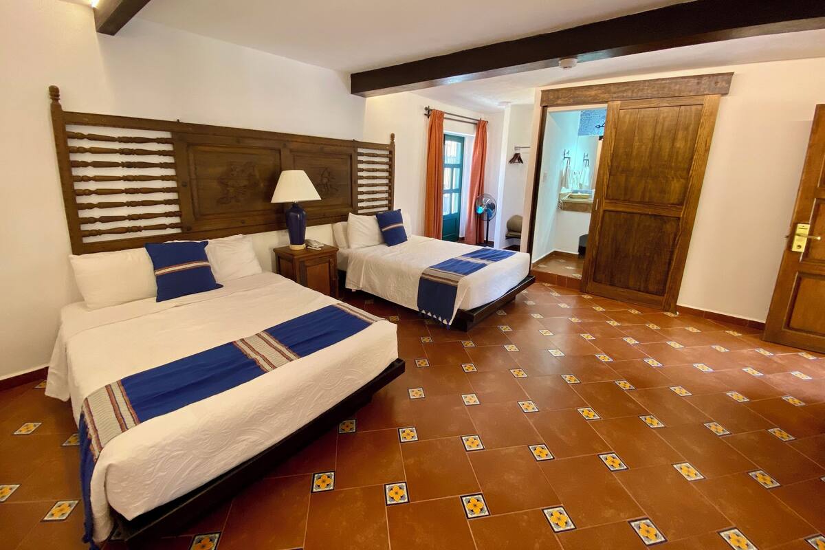 Een hotelkamer met twee bedden, een houten hoofdbord, een nachtkastje met een lamp, en een badkamer die door een open deur zichtbaar is.