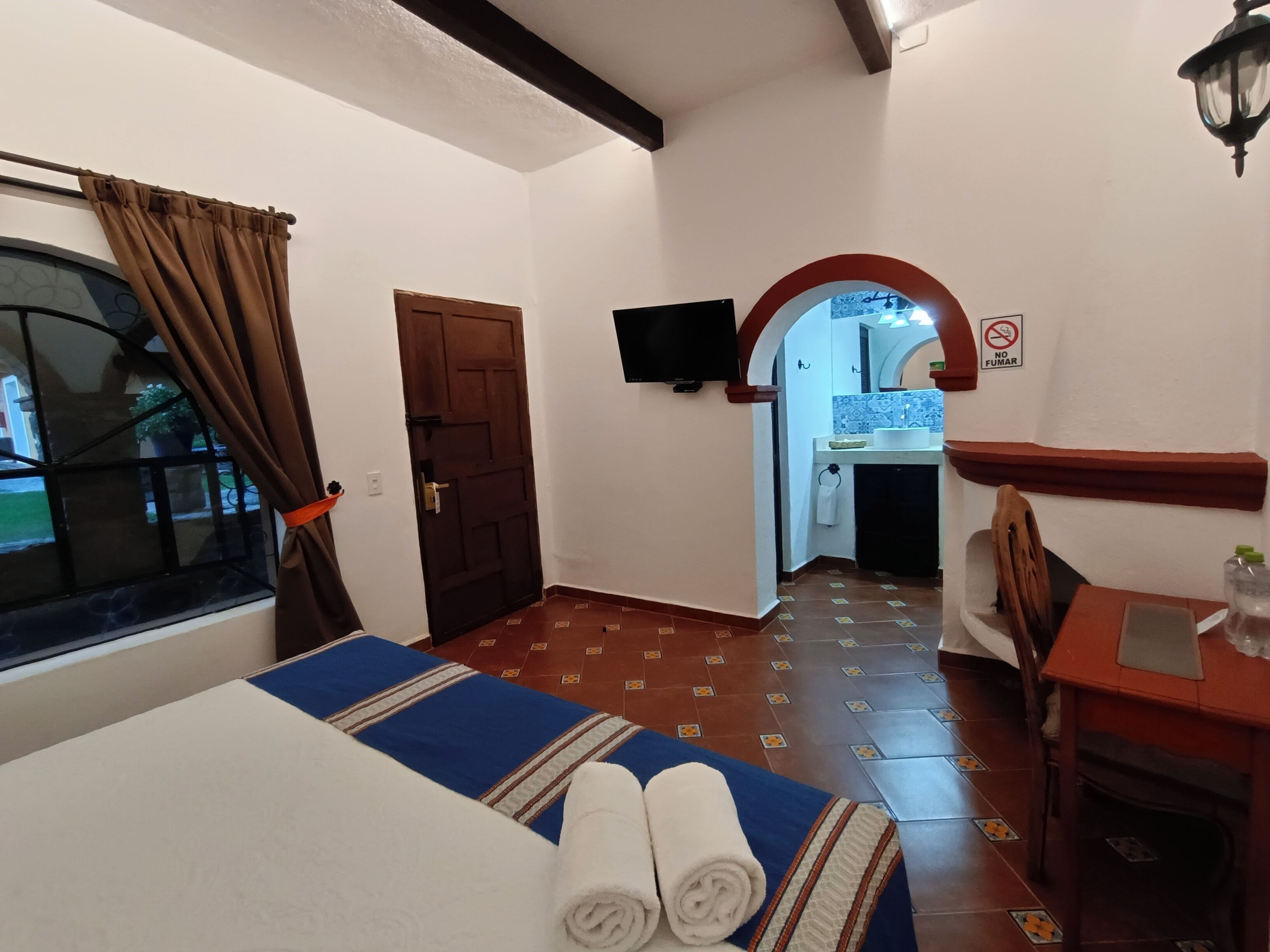 Une chambre d’hôtel avec un lit, une fenêtre avec des rideaux, une porte, un téléviseur fixé au mur et une vue sur la salle de bain.