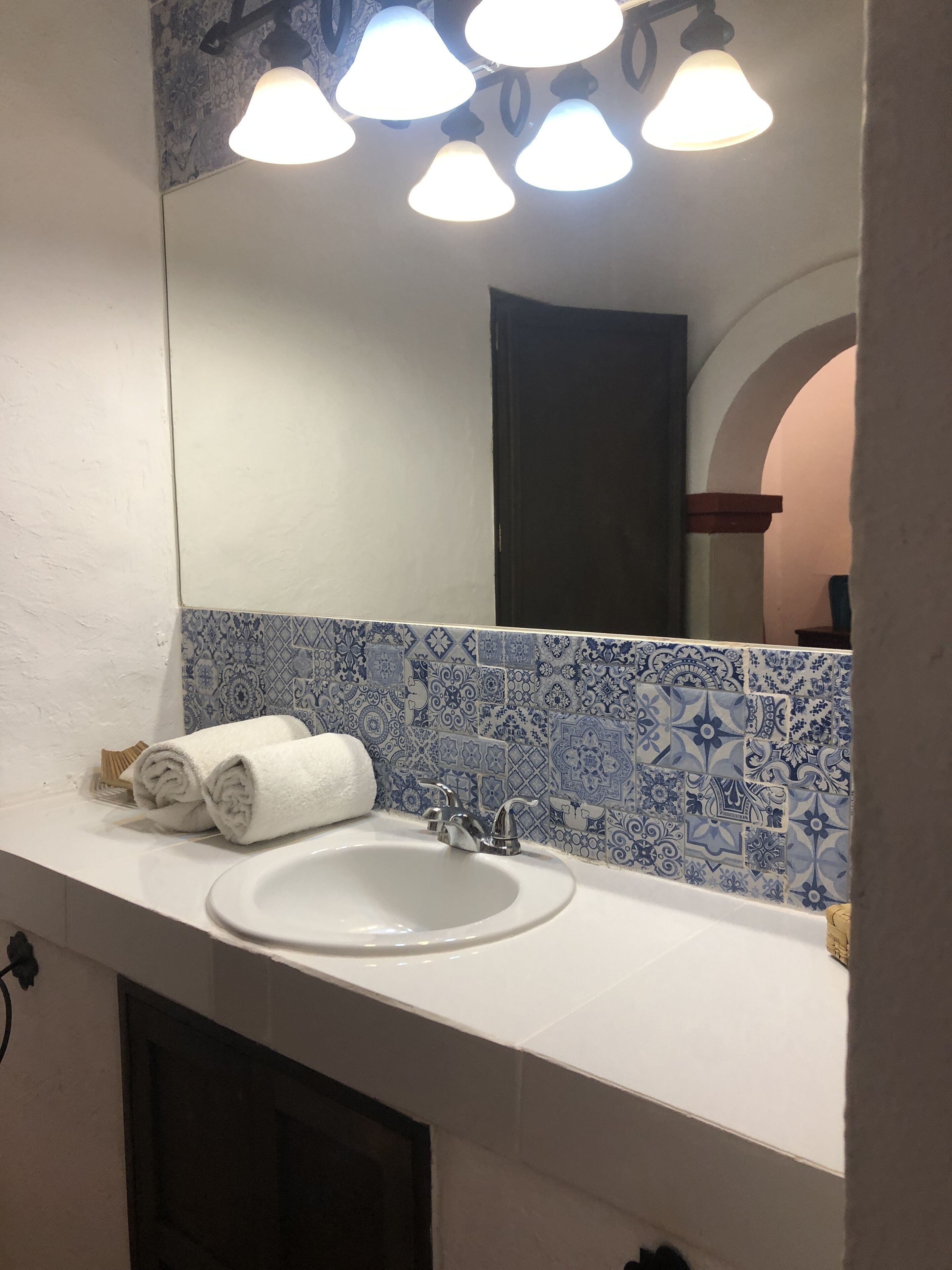 A bathroom with a white sink, blue patterned tiles, and a mirror with lights above.