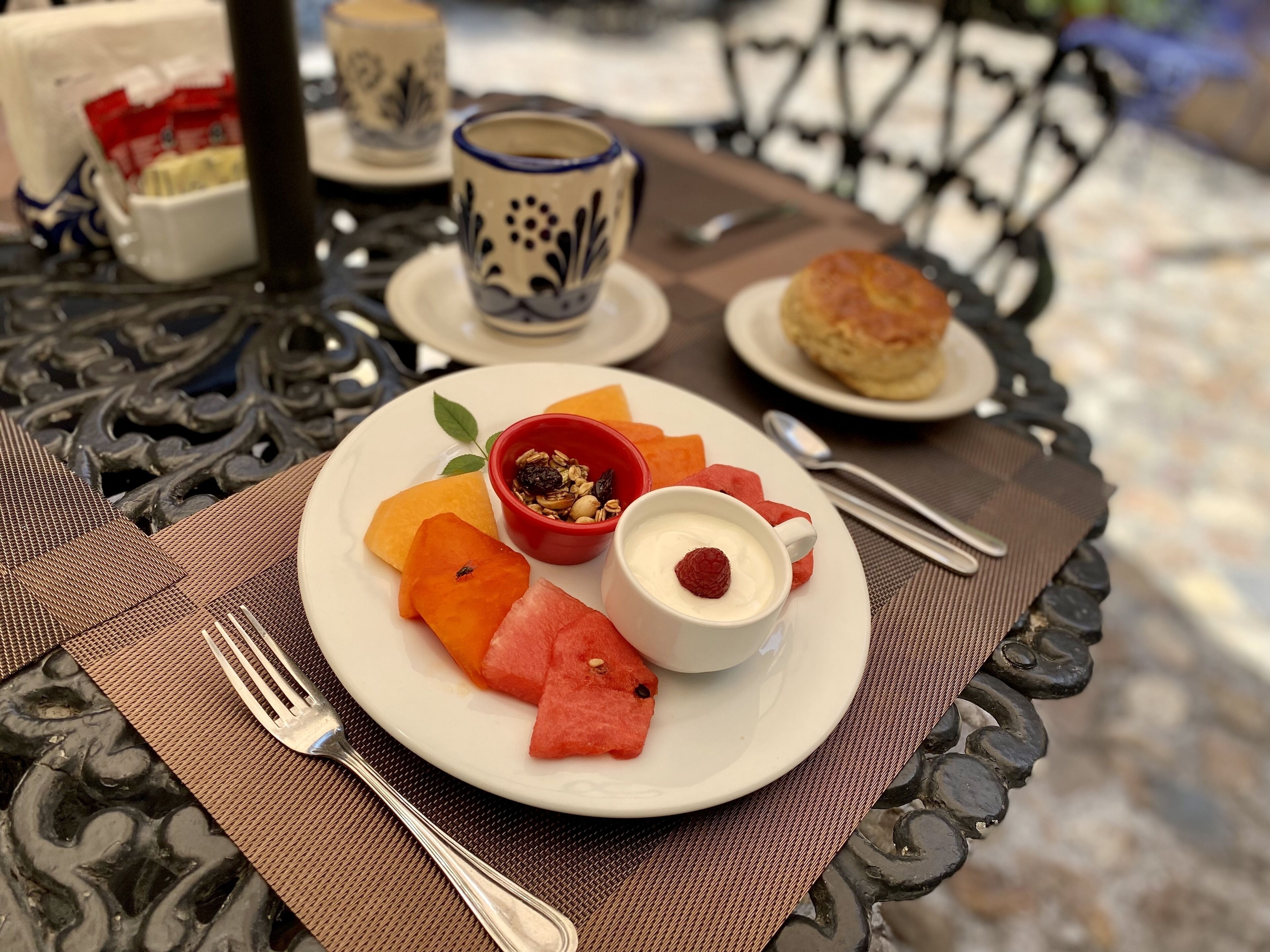 A table with a plate of food including watermelon, a bowl of yogurt with a raspberry, and a biscuit.