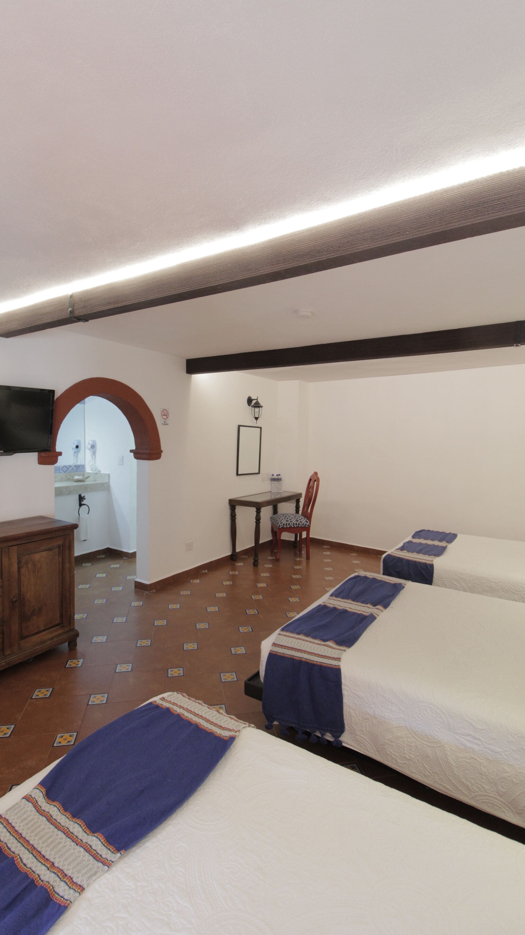 Habitación de hotel con cama, escritorio, silla, televisión y baño visible a través de un arco.