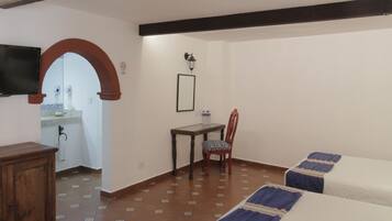 Habitación de hotel con cama, escritorio, silla, televisión y baño visible a través de un arco.