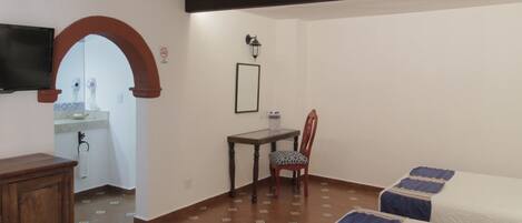 Une chambre d’hôtel comprenant un lit, un bureau, une chaise, une télévision et une salle de bain visible à travers une arche.