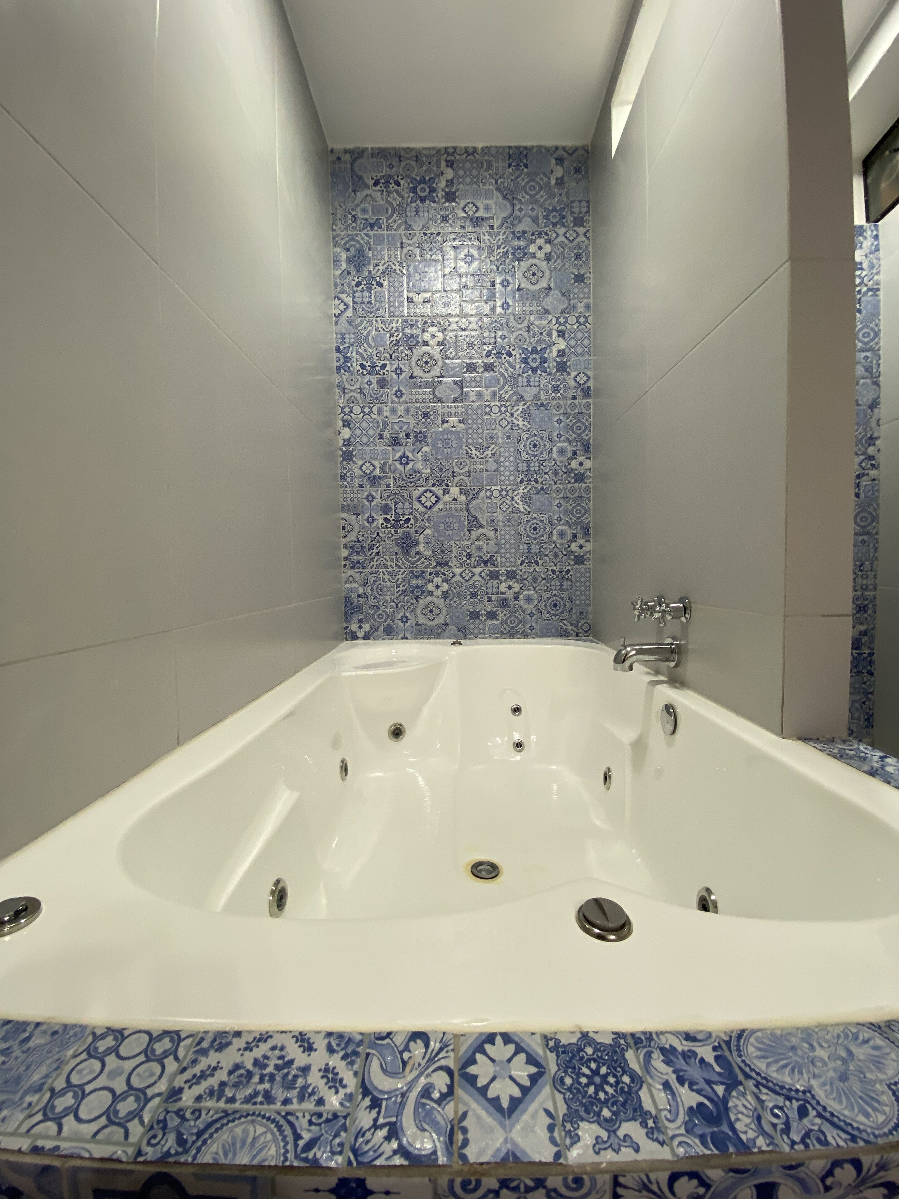 Un baño con bañera independiente, paredes con azulejos y un borde de baldosas estampadas.
