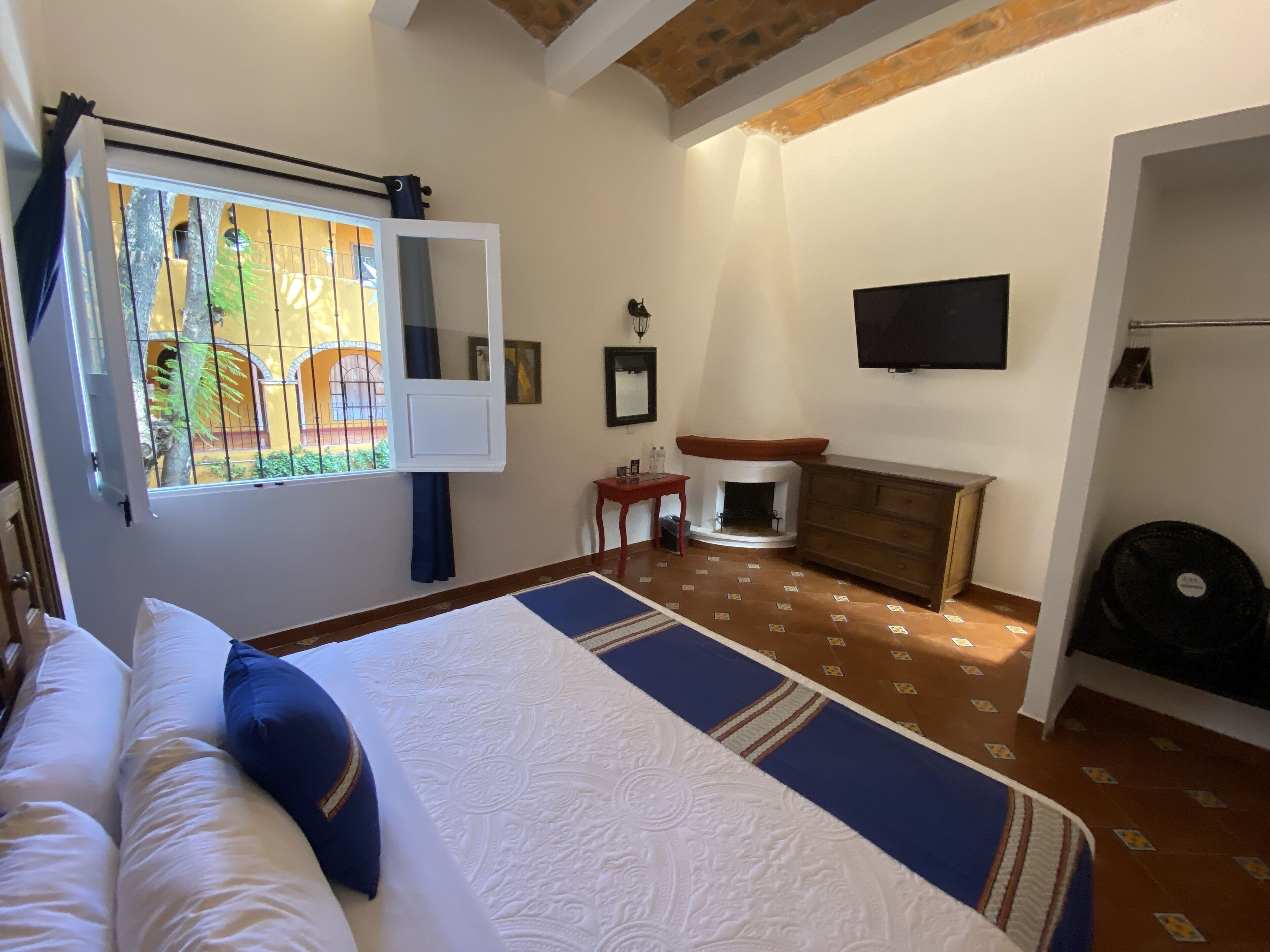 Un dormitorio con una cama grande, chimenea, televisor y ventana con cortinas.