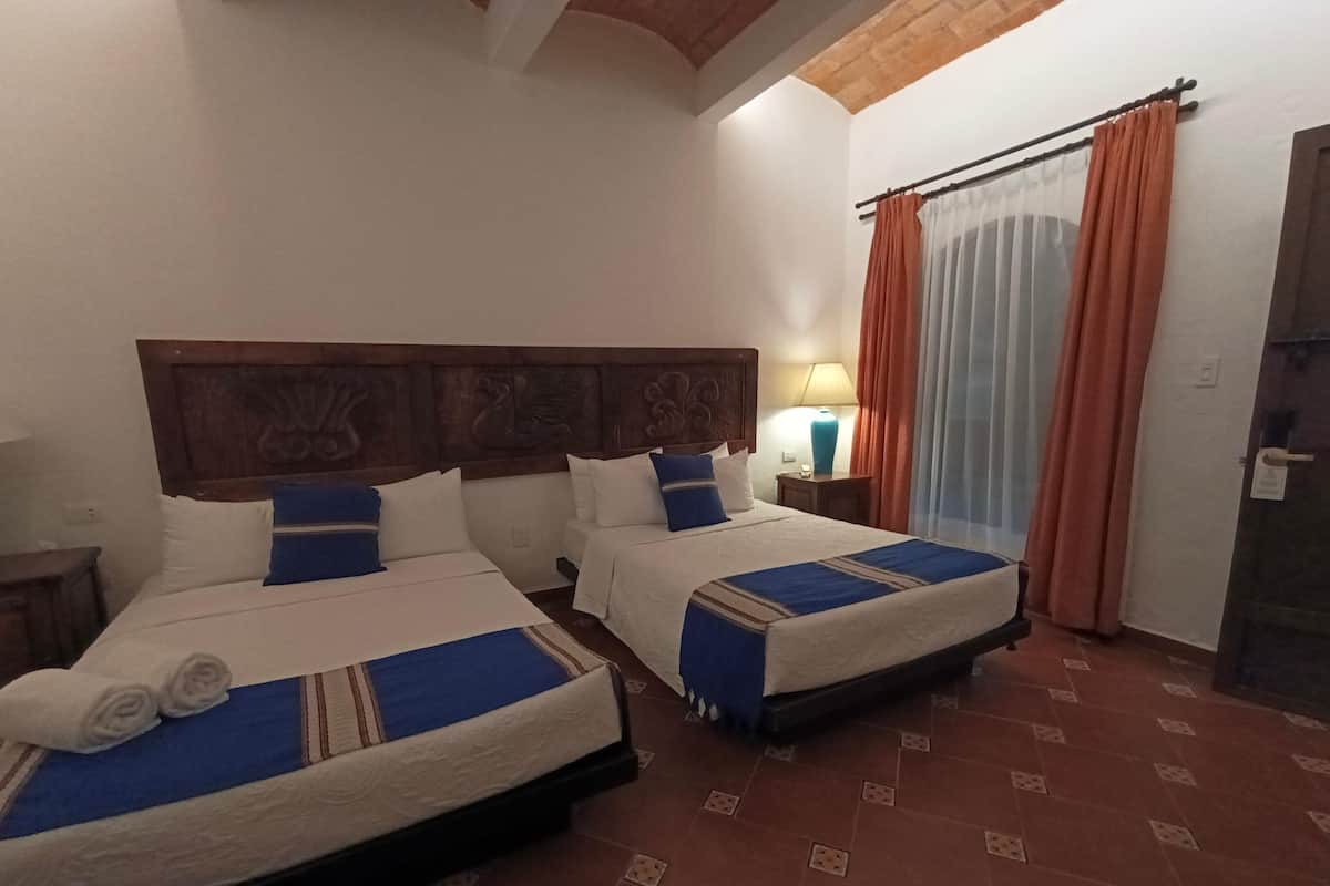 Een hotelkamer met twee bedden, een houten hoofdeinde, een nachtkastje met lamp en een deur voorzien van gordijnen.