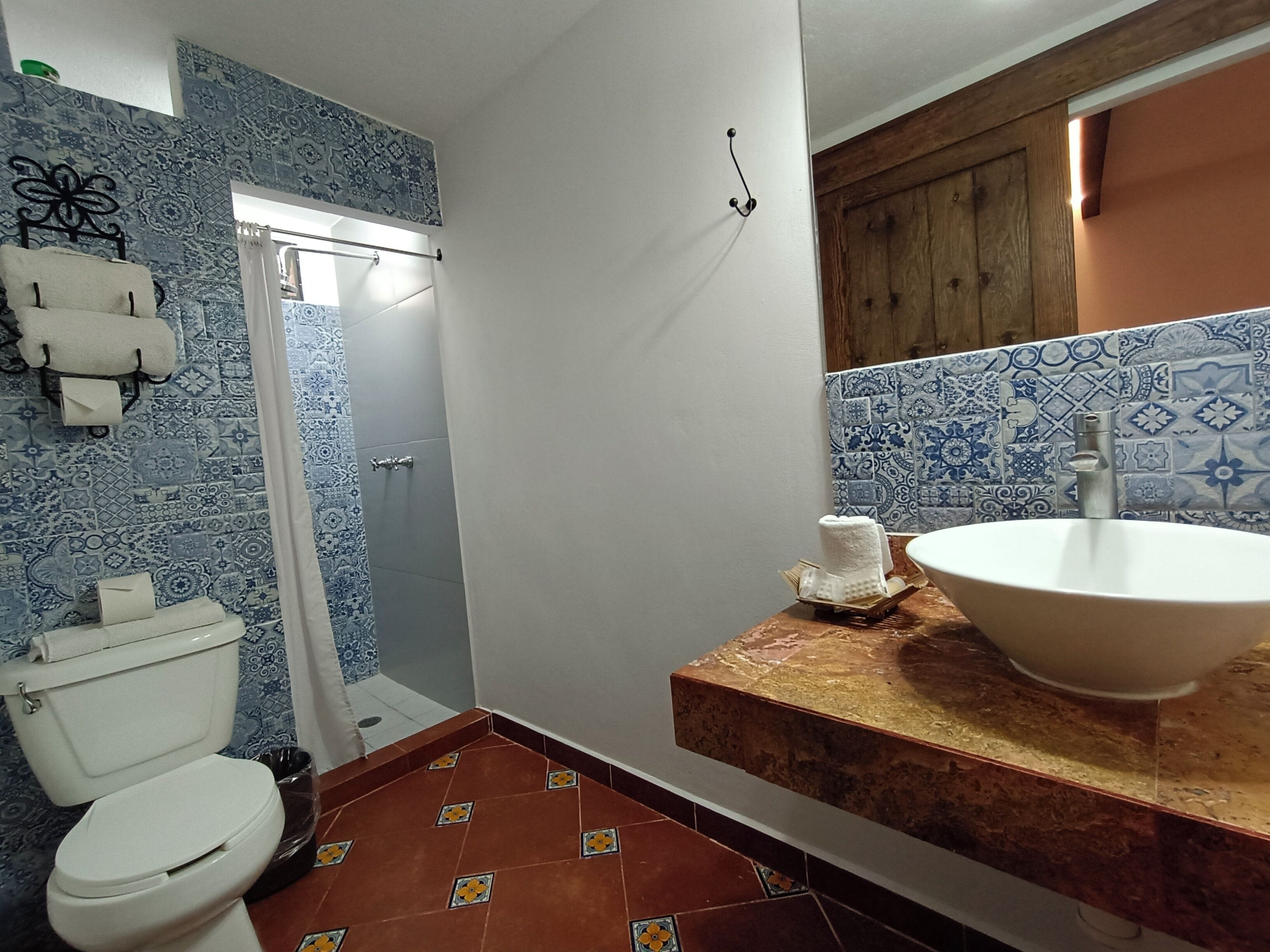 Une salle de bain avec des toilettes blanches, une douche avec un rideau, un lavabo avec un plan de toilette en marbre et des carreaux bleus et blancs à motifs sur les murs.